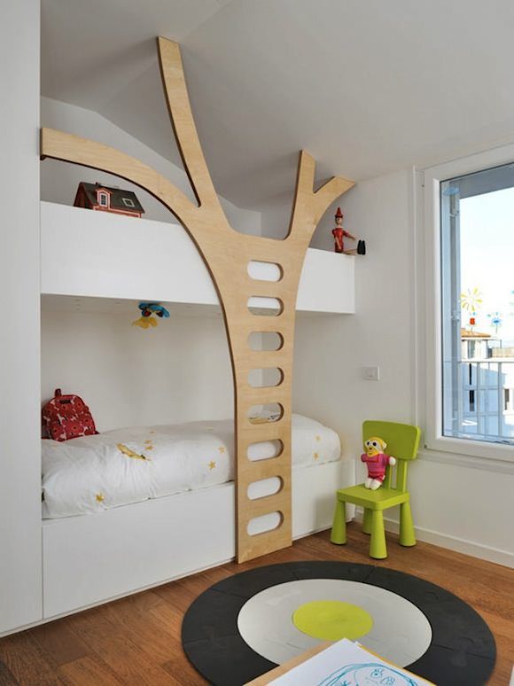 A small but edgy kids' room with built in bunk beds, with neutral bedding, a plywood staircase and a chair plus a bright rug is a pretty and lovely space