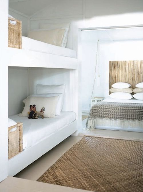 A neutral room with a large bed with neutral bedding, built in bunk beds with white and neutral bedding, baskets for storage is an airy and chic space