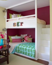 a bright kids’ room with a burgundy accent wall, built-in bunk beds, a ladder and colorful bedding, a dark-stained table and chairs