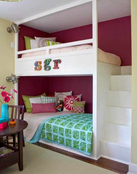 a bright kids' room with a burgundy accent wall, built-in bunk beds, a ladder and colorful bedding, a dark-stained table and chairs
