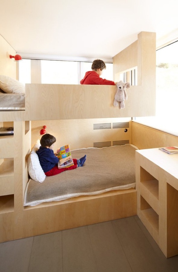 A minimalist kids' room with sleek plywood bunk beds built in, a ladder and a desk with open storage is a cool space filled with natural light