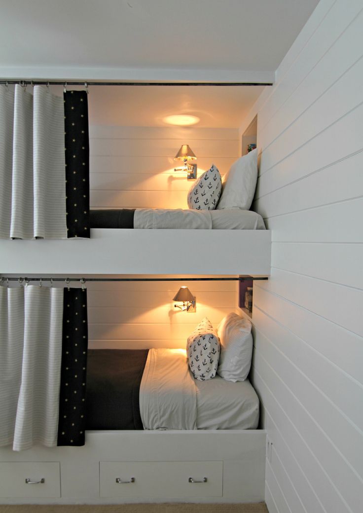 A white kids' room with built in bunk beds, black and white bedding and curtains, sconces on the walls for more coziness