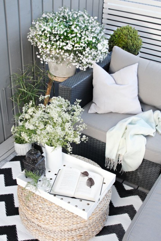 a summer Scandinavian terrace in black and white, with dark furniture, blooms and greenery in pots and a cool ottoman