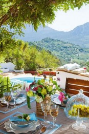 a bright summer terrace by the pool, with cushions and pillows and a bright dining zone with bold blooms and placemats with blue edges