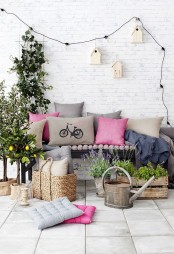 a bright and fun summer terrace with a black bench, colorful pillows, pallets and boxes with greenery and blooms, a garland and birdhouses for decor