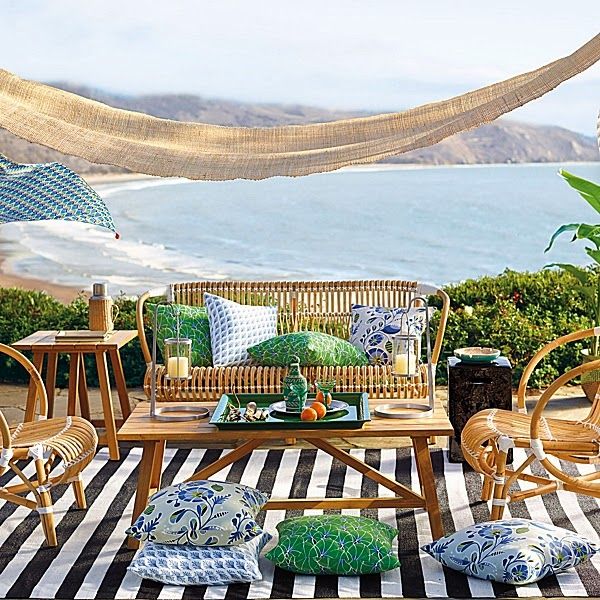 A bright and bold summer terrace with a cool sea view, a striped rug, rattan furniture, colorful textiles is super welcoming