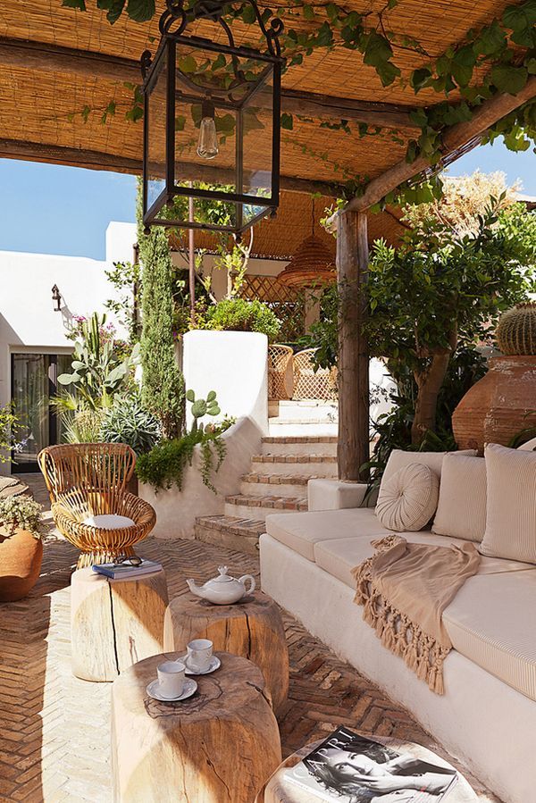 A neutral Mediterranean terrace with neutral furniture, wooden tables, a rattan chair and lots of greenery around
