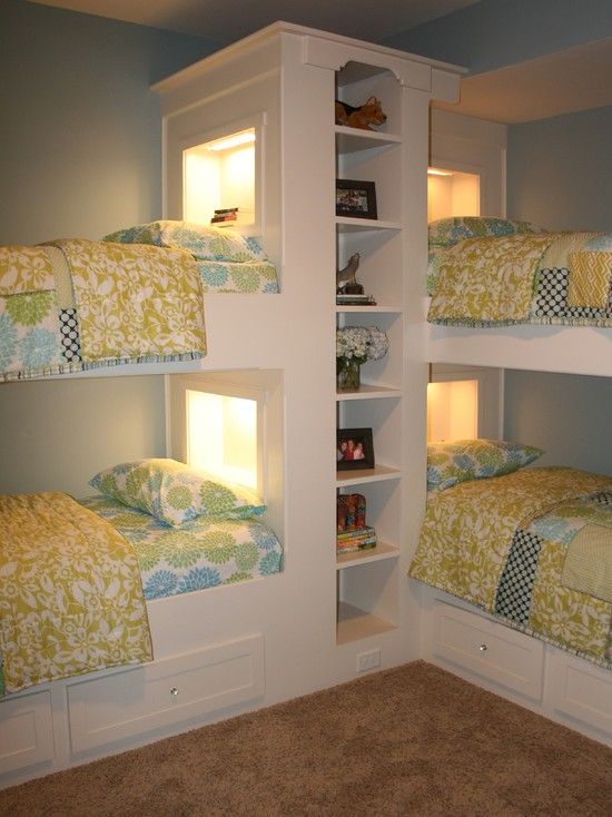 A traditional pastel bedroom with white built in bunk beds and a shelving unit in the center, built in lights and bright bedding