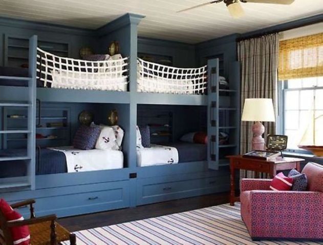 A seaside kids' room with navy built in bunk beds, a vintage table and a chair, a pink chair and some printed curtains