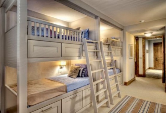 a farmhouse whitewashed kids' room with four built-in bunk beds and ladders, pastel bedding and a striped rug