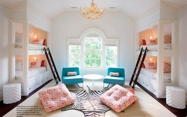 A neutral and refined kids' room with four built in bunk beds, ladders, sconces and bold bedding, turquoise chairs and orange cuhsions