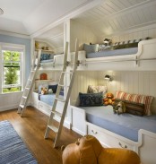 a white farmhouse kids’ room with four built-in bunk beds and pastel and bright bedding, ladders, rugs and cool toys