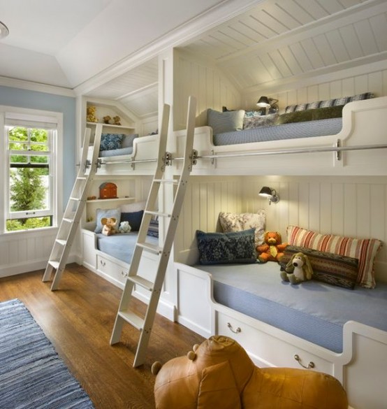 a white farmhouse kids' room with four built-in bunk beds and pastel and bright bedding, ladders, rugs and cool toys