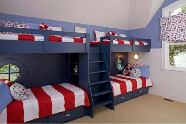 A seaside kids' room with navy built in bunk beds and bright bedding, porthole windows and bright curtains