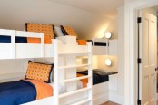 a pretty white kids’ room with four built-in bunk beds, with bright navy and orange bedding is a lively and cool space