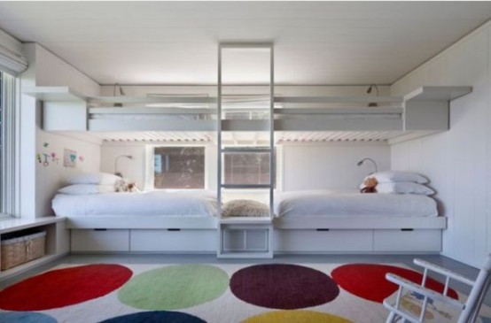 a white kids' room with built-in bunk beds, a windowsill storage bench, a bright rug, a ladder and some chairs