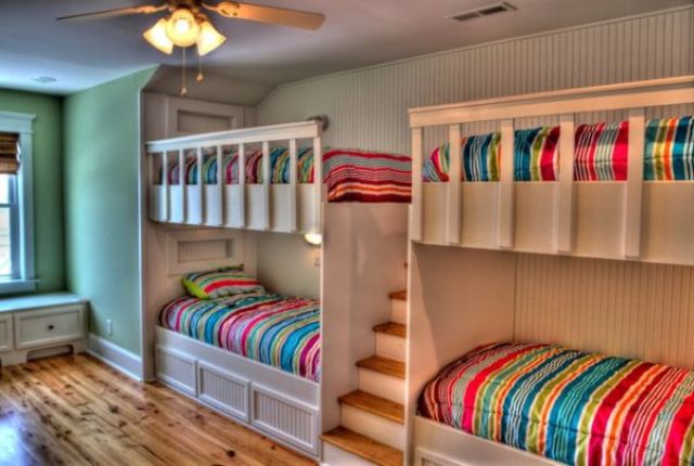 A neutral kids' room with a green accent wall, white built in bunk beds and bright bedding is amazing for kids
