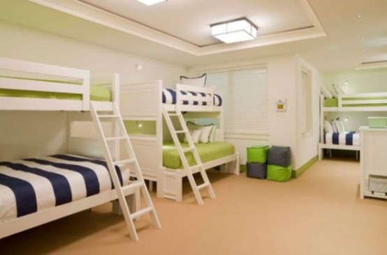 a large neutral kids' room with three bunk beds in white, with navy, white and green bedding and lights on the ceiling
