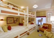 a bright kids’ room in yellow, red and white, with four built-in bunk beds, bright bedding, an orange chair, bright yellow and red textiles