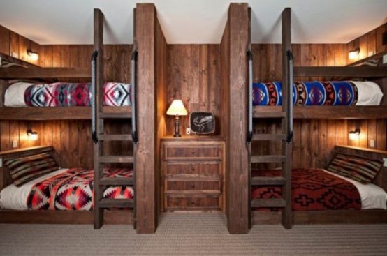 a dark-stained wood clad kids' room with built-in bunk beds, with ladders, a dresser in the center and wall sconces