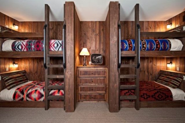 A dark stained wood clad kids' room with built in bunk beds, with ladders, a dresser in the center and wall sconces
