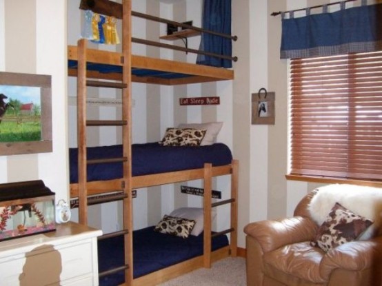 a small neutral kids' bedroom with a triple bed, a leather chair and a dresser, navy bedding and a navy curtain