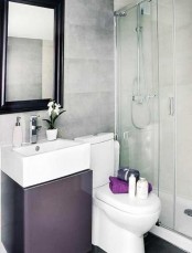 a small minimalist bathroom with concrete walls, a shower space, a purple vanity and a mirror in a dark frame