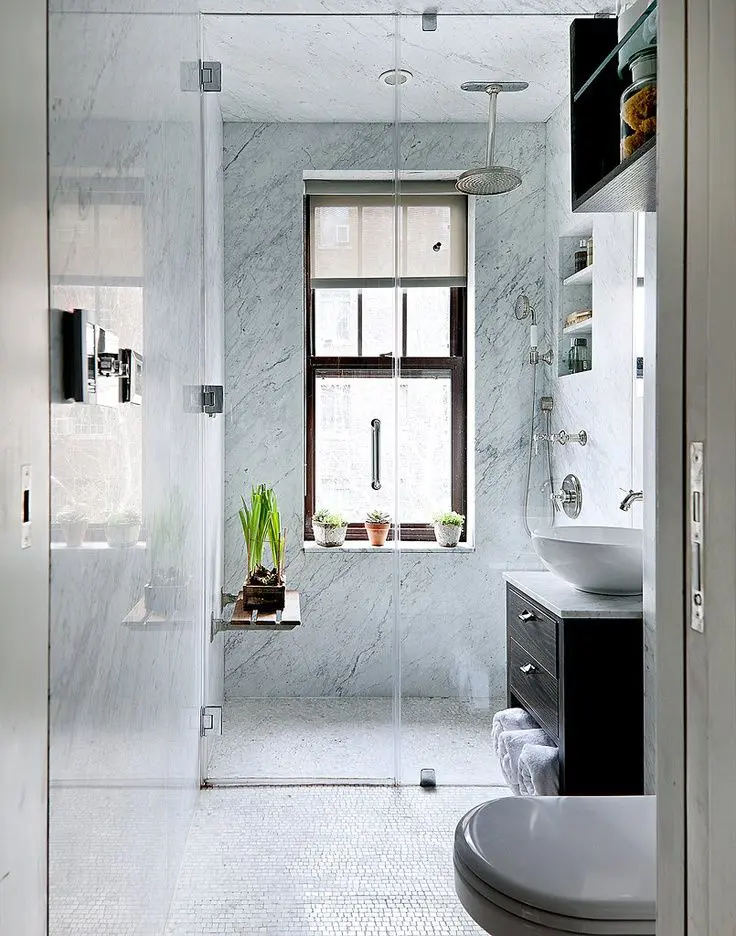 A small bathroom with blue stone tiles in the shower, a dark stained vanity, potted greenery and built in shelves
