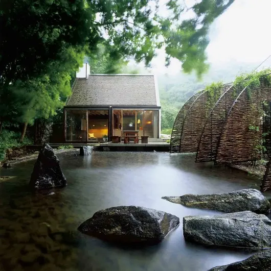 Zen-like Japanese garden house surrounded by peaceful greenery,  big natural stones and a stick private fence.