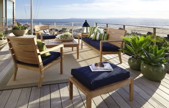 a beachy patio with light-colored wooden furniture, navy upholstery, candle lanterns and potted plants