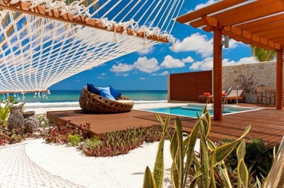 a beach deck with a pool, some contemporary furniture, a hammock and a gorgeous sea view