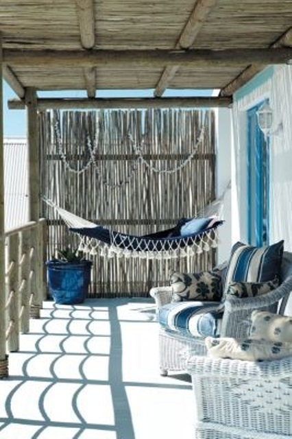 a beachy porch with wicker furniture, a hammock, blue and white textiles and some seashells for decor