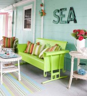 a colorful sea porch with mint walls, a neon green bench, colorful textiles, wicker tables and bright blooms