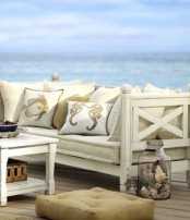 a seaside patio with vintage neutral furniture, neutral upholstery and printed pillows, jars with seashells and crates is very chic