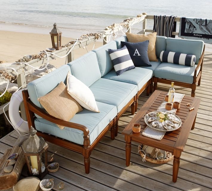 A beach patio with rich stained wooden furniture and blue upholstery, striped pillows, candle lanterns and seashells and rope for decor