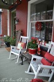 bright rustic Christmas porch decor with potted evergreens, a red wreath and a red bucket with a mini tree and red pillows