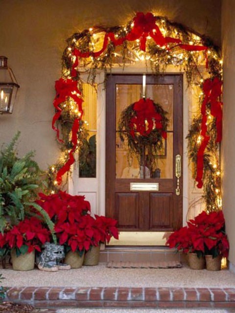 a super bright and bold Christmas porch with red ribbons and bows, lights, a wreath with poinsettias, greenery and poinsettia arrangements in pots