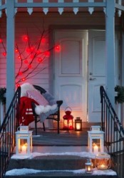 a modern Christmas porch with a chair with pillows, blankets, a tree with red lights and lots of candle lanterns