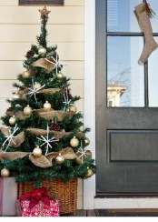 a Christmas tree with gold ornaments, pinecones, snowflakes in a basket is a lovely rustic decoration for your porch