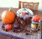 fall table decor with acorns, faux and natural pumpkins, a glass jar with pinecones, leaves and faux fruits and veggies