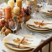a chic and natural fall tablescape with fresh fruits, dried blooms, twigs, candles and fall leaves to mark each place setting