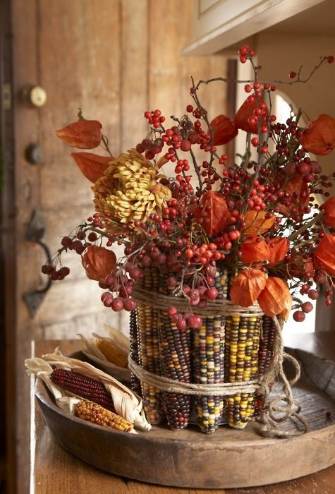a fall centerpiece of berries and dried blooms covered with corn cobs and husks for a more natural look