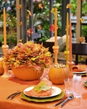 a fall centerpiece of a pumpkin as a vase with fall leaves and orange candles is easy to recreate yourself