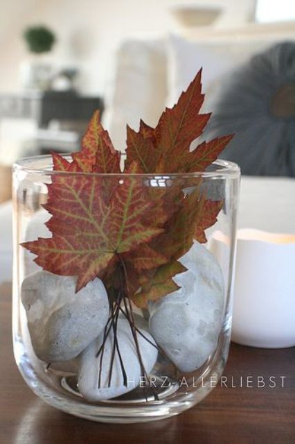 a glass with pebbles and fall leaves is a simple and cool decoration for fall parties with a natural feel