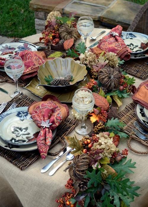 a traditional fall tablescape with vine, faux berries, fruits and leaves, woven placemats and a metal bowl in the center