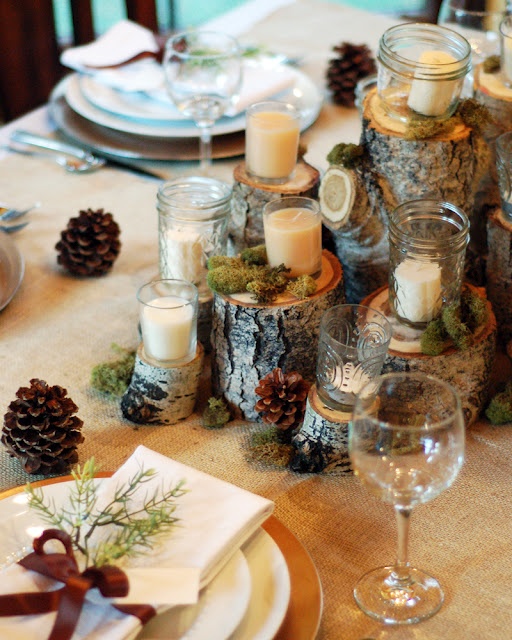 a rustic fall tablescape with a tree stump, candles and pinecones centerpiece and gold chargers and greenery for each place setting