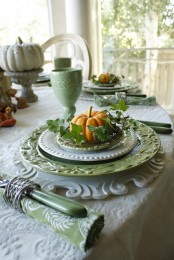 a pastel fall tablescape with green plates, napkins and cutlery, printed tablecloths and faux pumpkins and greenery