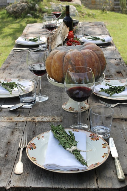 a fall tablescape with an uncovered table, a large pumpkin centerpiece, printed plates and greenery