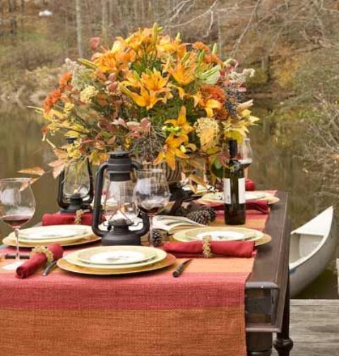 a colorful fall tablescape with a bright tablecloth, red napkins, pinecones, a lush arrangement of bold blooms and fall leaves