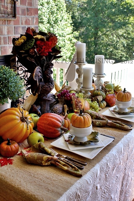 A vintage inspired fall tablescape with printed napkins, faux pumpkins, berries and veggies, candles in neutral candle hohlders and a centerpiece with bold blooms